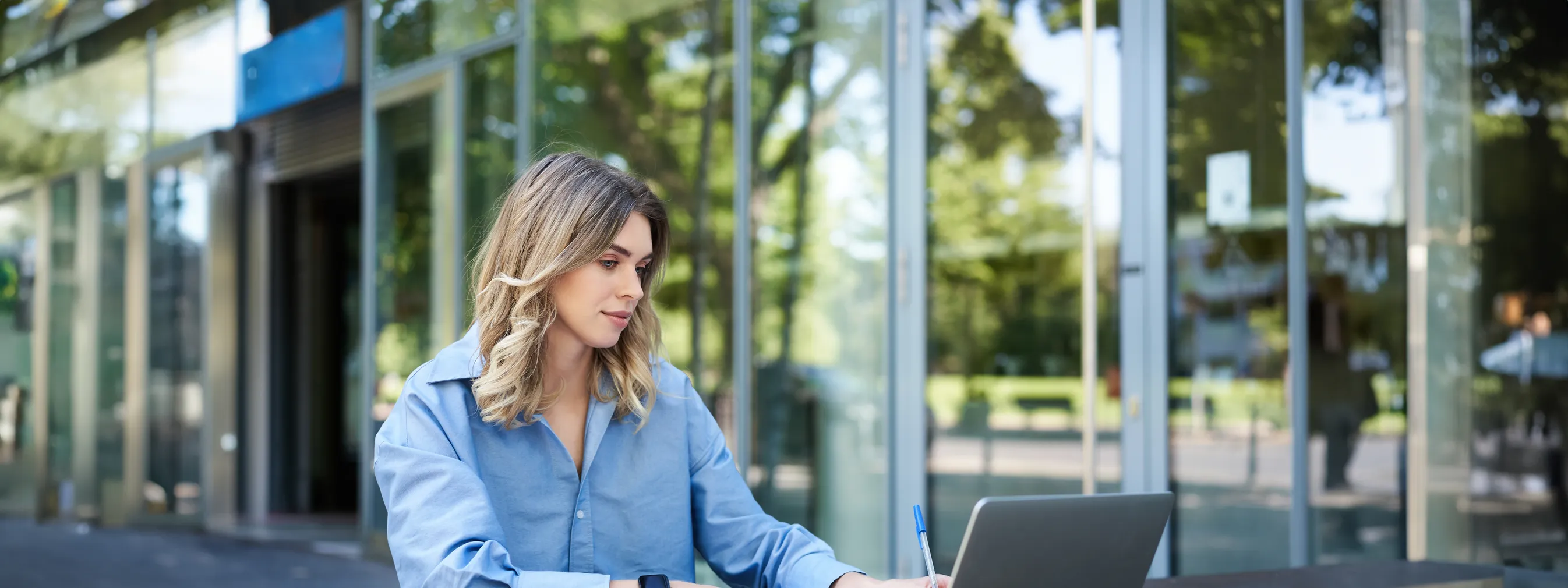 A person working at a laptop outside a glass-fronted office.